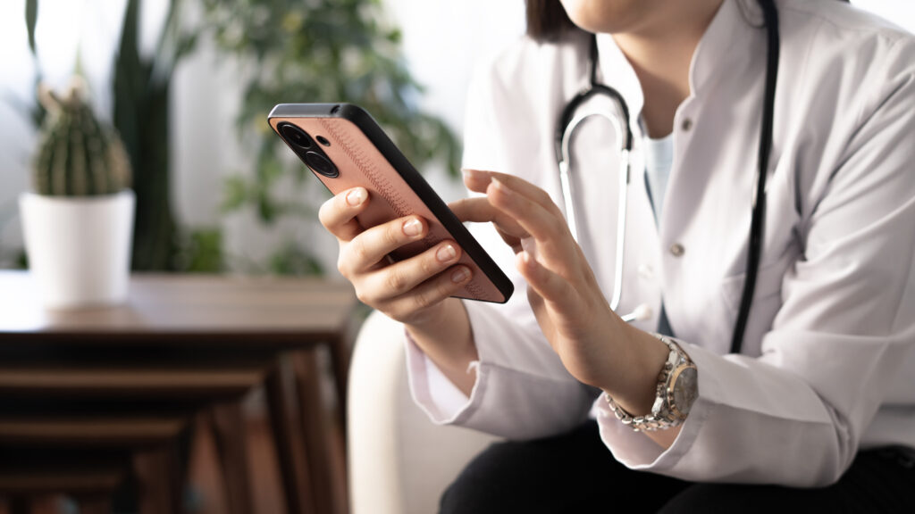 Female doctor hand using smartphone while sitting on chair in office