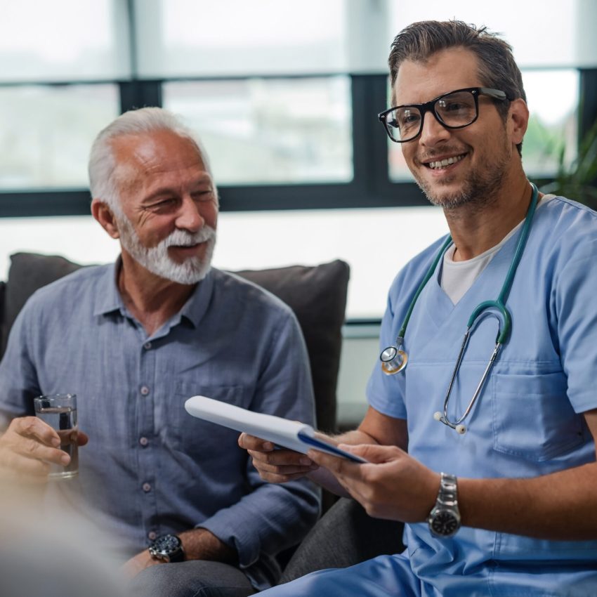 Happy male doctor visiting senior patients at home and going through medical documents.